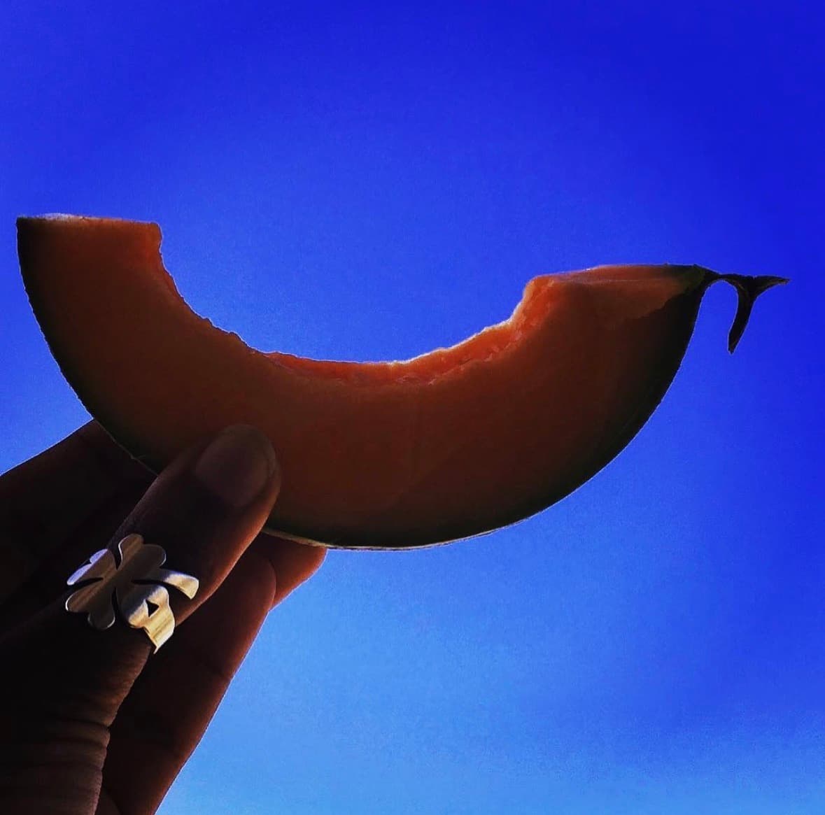 Hand holding a melon slice against a vivid blue sky